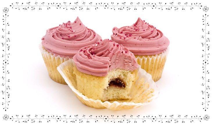 Imagem de um cupcake de massa clara e obertura rosa. O recheio é de chocolate e estão em uma forminha branca.
