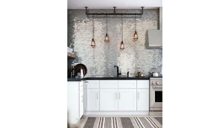 Na foto há uma cozinha em que as luminárias, assim como a torneira, são em estilo industrial, com cores escuras e fios aparecendo.