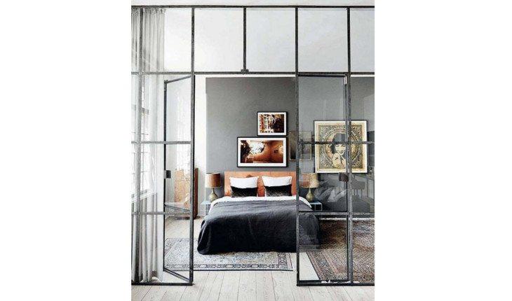 Na foto há um quarto que sua divisória é uma janela de indústria com vidros e as molduras em preto.