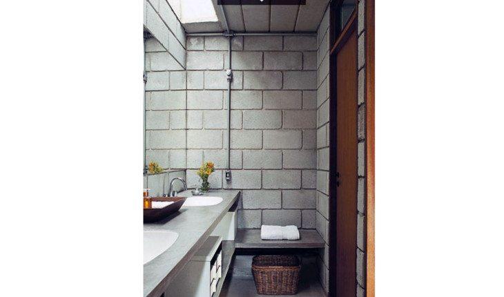 Na foto há um banheiro feito com tijolos de construção, da cor cinza, e canos pretos.