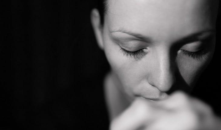 A foto em preto e branco mostra uma mulher rezando de olhos fechados com as mãos unidas