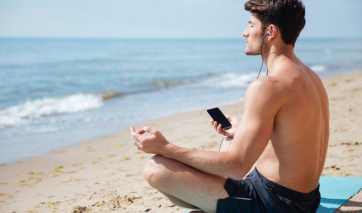 A foto mostra um homem praticando o mindfulness em uma praia