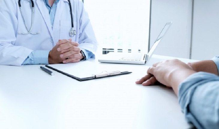 Na imagem, o médico e paciente estão com as mãos cruzadas na mesa, com caderneta, e outros objetos. Dispositivo intrauterino.