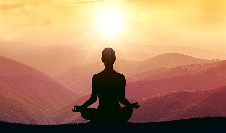 A foto mostra uma mulher praticando mindfulness em uma montanha