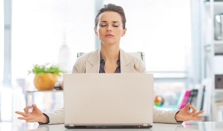 A foto mostra uma mulher sentada na frente do seu notebook praticando mindfulness