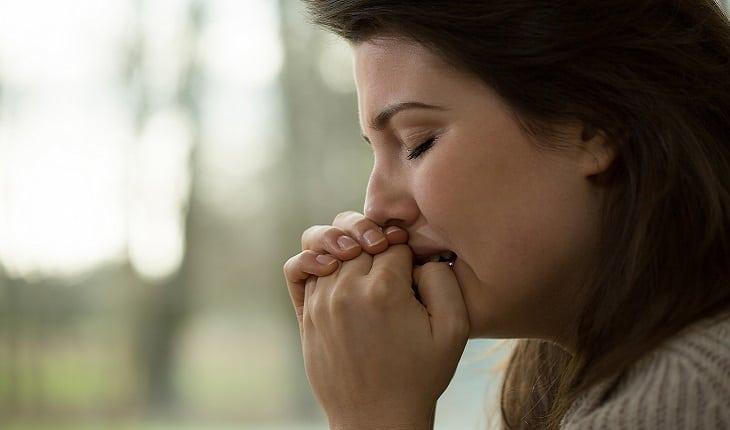 A foto mostra uma mulher rezando com cara de choro