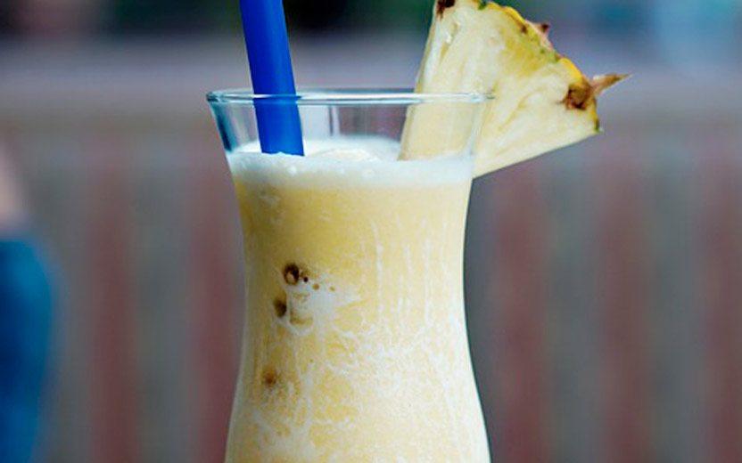 Sucos com colágeno. Na foto, um copo com suco de abacaxi com canudo e um abacaxi enfiado no copo