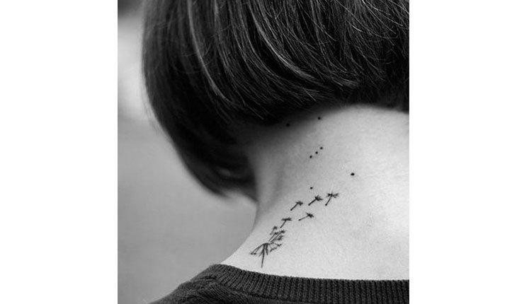 Na foto há uma mulher de costas com o cabelo curto com uma tatuagem de dente de leão tatuada no pescoço.