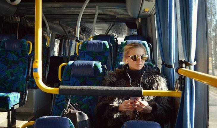 Fotografia de uma mulher viajando em um ônibus enquanto utiliza celular.