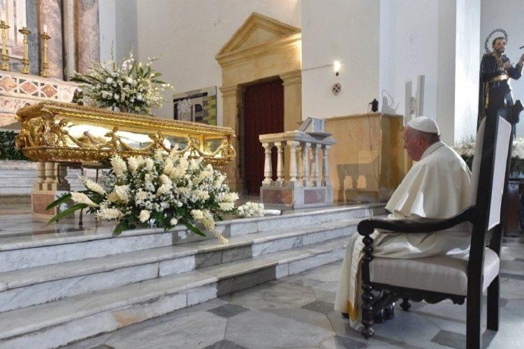 Na imagem, o papa francisco está sentado na cadeira contemplando o caixão com algum santo. Nossa Senhora de Chiquinquira