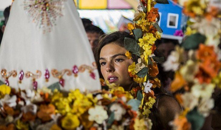 Na imagem, Isis Valverde olha para a santa, que está de costas, com flores amarelas. Nossa Senhora de Nazaré.
