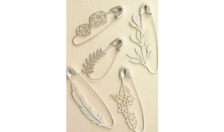 Na foto há diversos broches pratas em formato de alfinete com detalhes de flores e folhas nos desenhos.