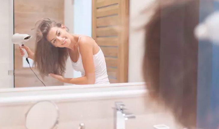 Bad Hair day. Na foto, uma mulher de cabelos castanhos secando-os em frente ao espelho