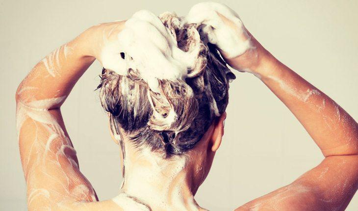 Na foto há uma mulher lavando os cabelos de costas.