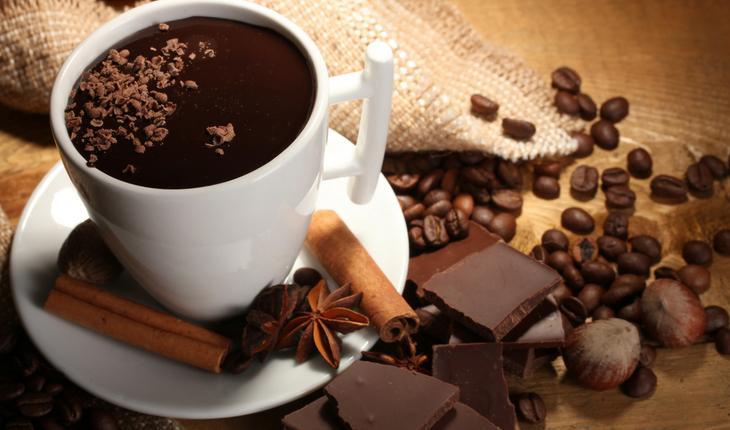 Xícara branca com chocolate quente e pedaços de chocolate e grão de café ao lado