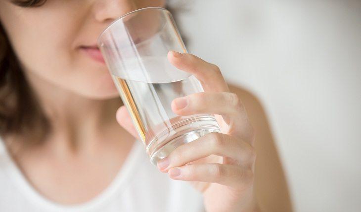 mulher bebendo água em copo transparente