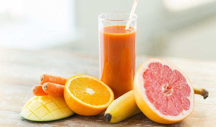 copo com suco ao lado de laranja, banana, cenoura e manga