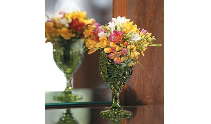 Na foto há um vaso de vidro com flores amarelas e rosas