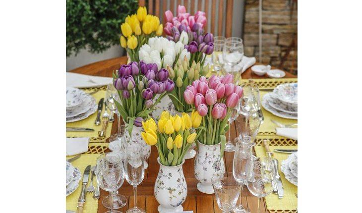 Na foto há uma mesa posta com vasos e flores.