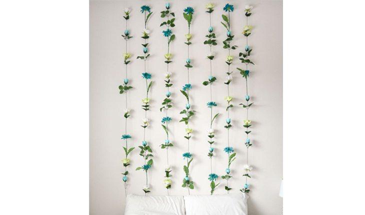 Na foto há uma parede com pêndulos de flores atrás de uma cama.