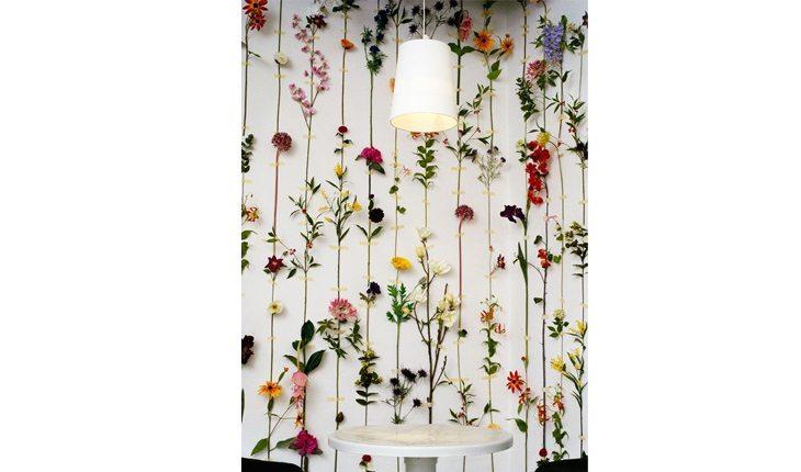 Na foto há uma parede com flores penduradas.