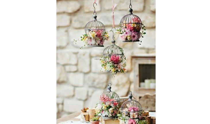 Na foto há uma mesa com gaiolas decorativas pequenas com flores.