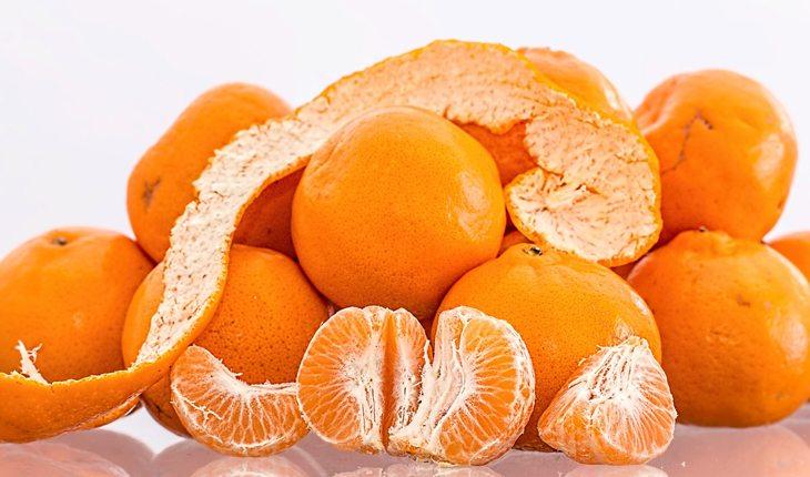 Na foto há diversas tangerinas e uma delas está aberta.