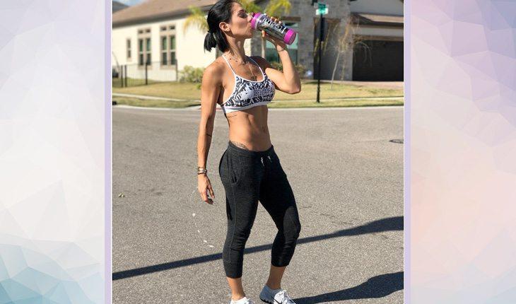 Moda fitness. Na foto, uma mulher com uma calça de moletom e um top de academia bebendo água