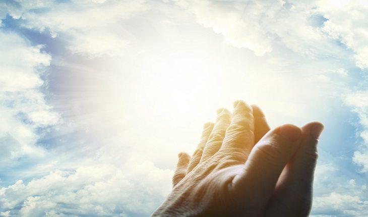 mãos femininas em posição de oração em direção ao céu