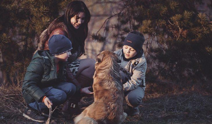 Na imagem, a mãe está com os dois filhos brincando com o cachorro. Frases abençoadas.