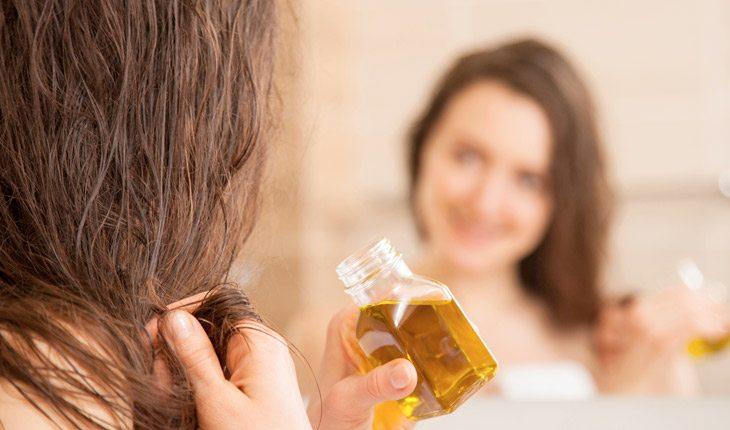 Na foto há uma mulher com um vidrinho de óleo de rícino passando-o nos cabelos.