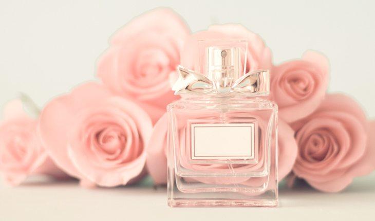 Perfumes para o verão. Na foto, vidro de perfume com rosas ao fundo