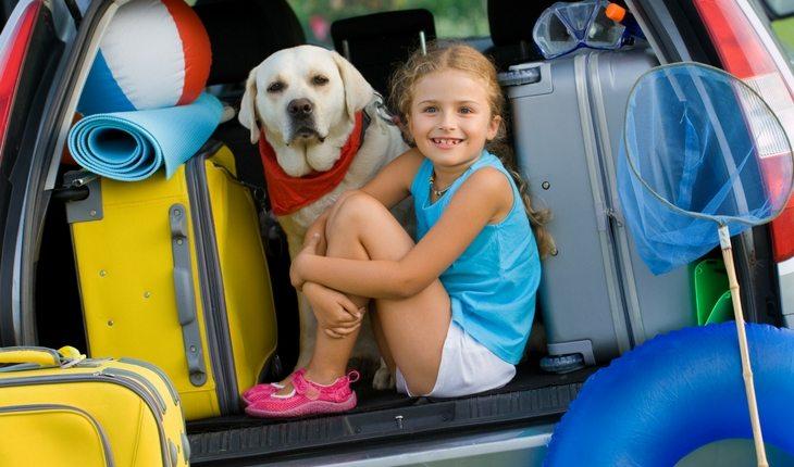 Menina e um cachorro dentro do porta mala de um carro antes de viajar