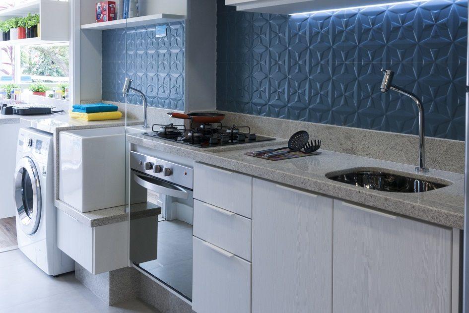 cozinha pequena com parede de azulejo azul, foto tirada na diagonal para aparecer a lavanderia acoplada à cozinha com uma máquina de lavar branca e uma janela cheia de vasos com plantas