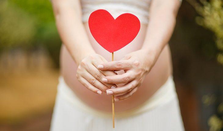 mulher grávida segurando coração vermelho em frente à barriga