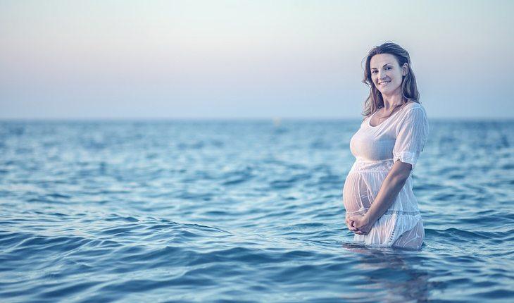 mulher grávida dentro de um lago com vestido branco olhando para a foto