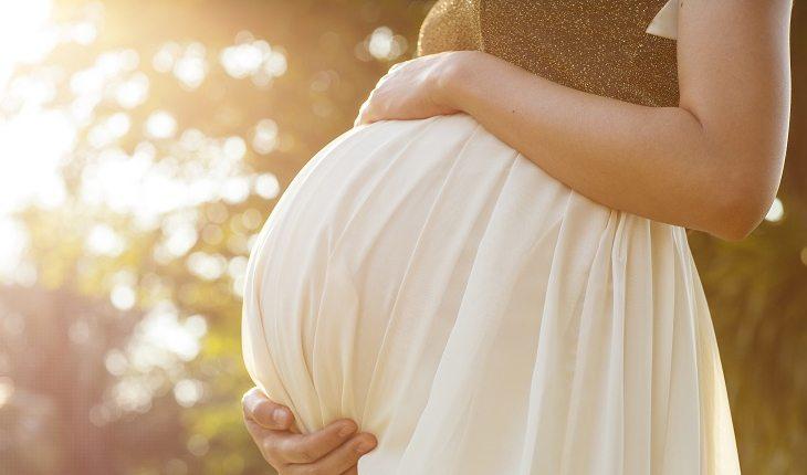 mulher grávida de vestido bege segurando a barriga
