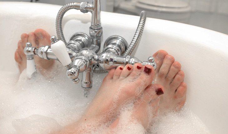 Na imagem, os pés de um casal está juntos na banheira com espuma. Falta de higiene.