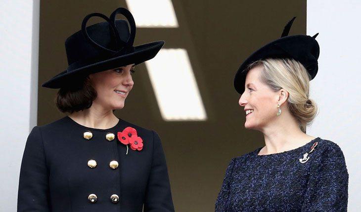 Kate Middleton com o cabelo curto e chapéu conversando com outra mulher loira