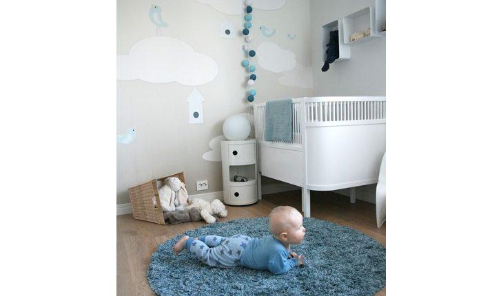 Quarto de bebê com tapete redondo azul, berço branco com enfeites em branco e azul