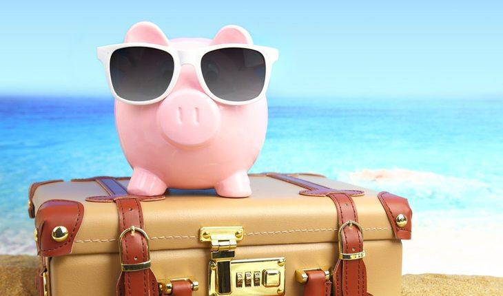 porquinho de dinheiro com óculos de sol em cima de uma mala na praia