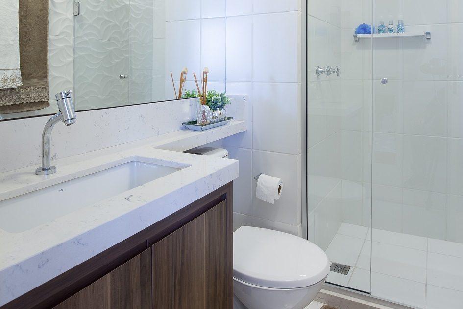 Projeto exemplo de banheiros que parecem ampliados com parede branca texturizada e grande espelho na parede oposta.