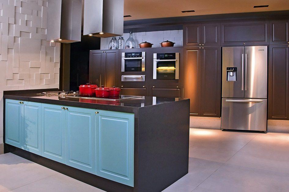 Cozinha retrô com eletrodomésticos modernos com forno embutido na parede de armários marrons e uma geladeira de 3 portas. Todos os eletrodomésticos são de aço inox prata.