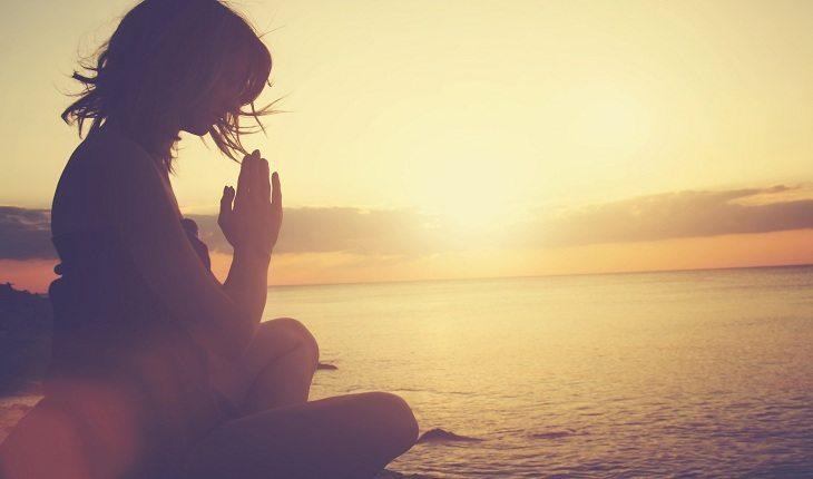 foto de uma pessoa orando ou meditando em uma praia, durante o pôr-do-sol