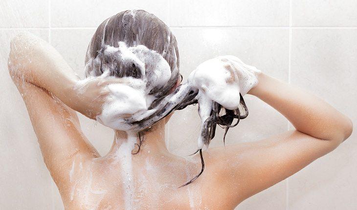 mulher lavando os cabelos castanhos com espuma de shampoo