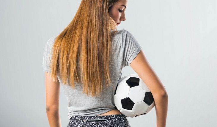 Menina de cabelo comprido segurando bola de futebol embaixo do braço