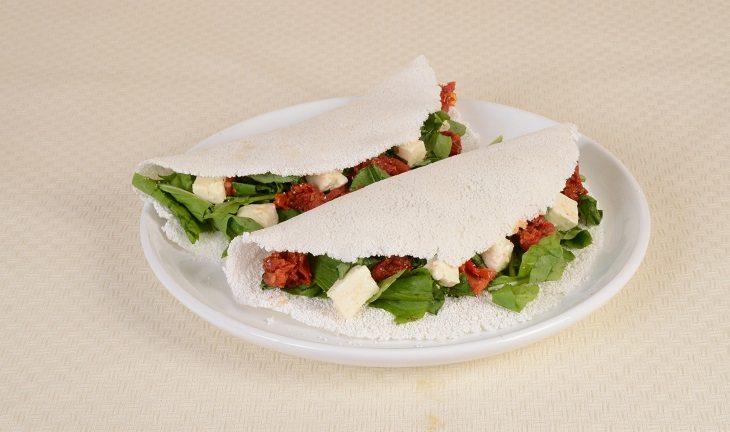 Prato branco redondo com duas tapiocas recheadas de rúcula e tomate seco.