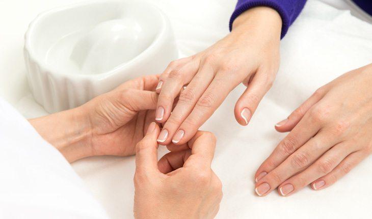 5 maneiras de fortalecer as unhas. Na foto, uma mulher com as mãos em uma mesa e outra pessoa segurando e olhando as unhas