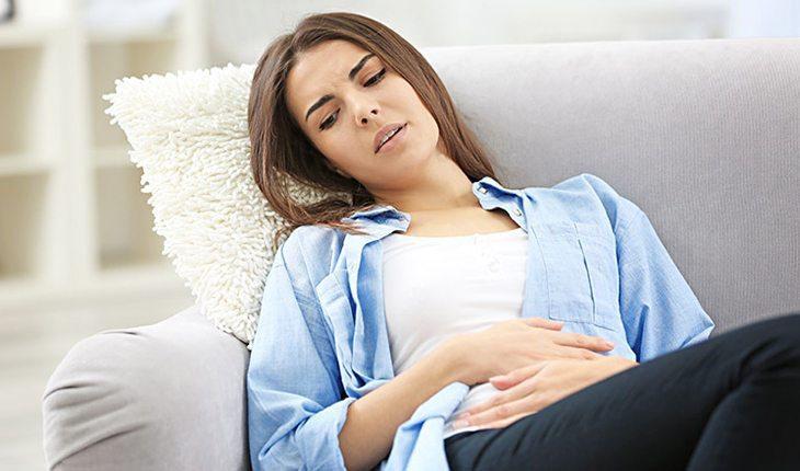 Primeiros sintomas de gravidez. Na foto, uma mulher sentada no sofá com as mãos na barriga