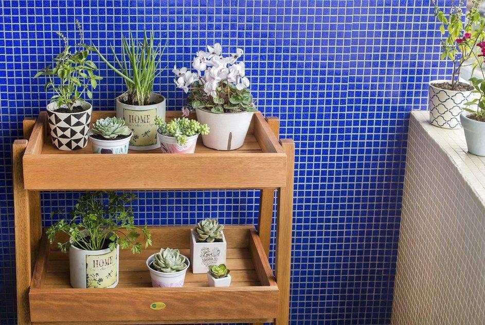 Uma varanda com uma horta vertical feita em uma estante com duas prateleiras com vasinhos de plantas.